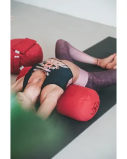 Yoga bolster rosso con pula di grano saraceno e fodera in cotone, rullo cilindrico per pratica restaurativa.